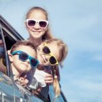 three kids wearing sunglasses sticking their heads out of a car window.