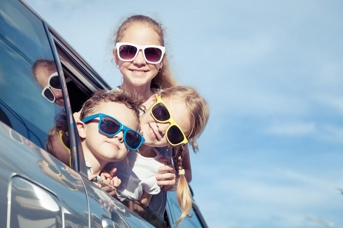 three kids wearing sunglasses sticking their heads out of a car window.